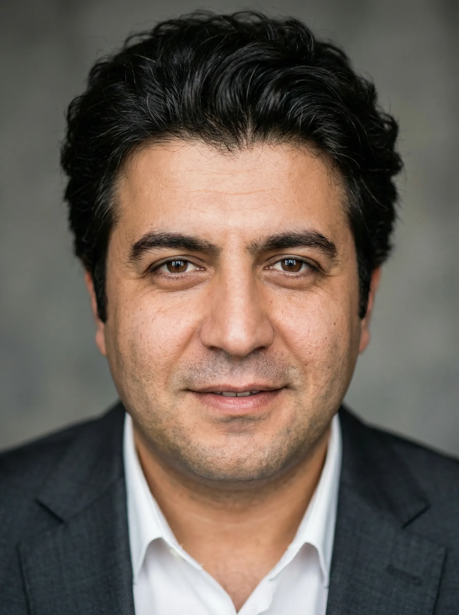 Professional headshot of a man in a charcoal blazer and white shirt against a soft gray background